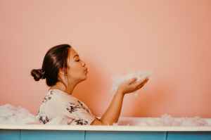 woman in a bath tub blowing bubbles